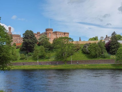 View of a castle on a hill, below a calm river with green banks and a spring-like sky, inverness,