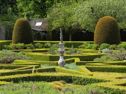A formal garden with symmetrically trimmed hedges and a central sculpture, all set in a verdant