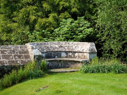 An old stone bench in a historic garden surrounded by green trees and plants, inverness, Scotland,