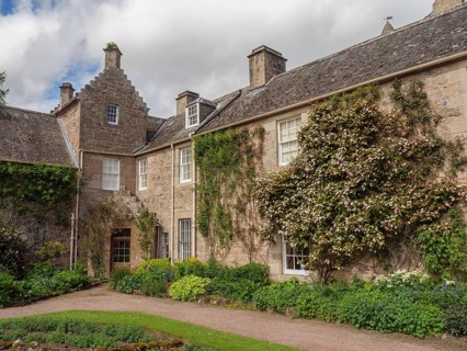 Stone house with climbing plants and windows, surrounded by flowers and garden, inverness,