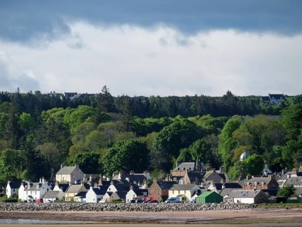 A small village of houses on the coast, surrounded by dense trees and clouds in the sky, inverness,