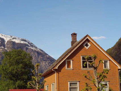 A brown wooden house with a high roof in front of a mountain panorama under a clear sky, Eidfjord
