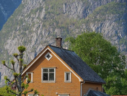 Wooden house in front of steep rock faces and green landscape under a clear sky, Eidfjord NOR 3
