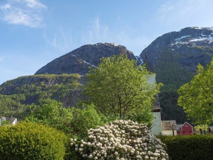 A church behind blossoming trees and bushes with towering mountains in the background, Eidfjord NOR