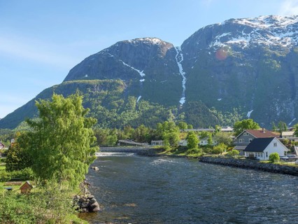 An idyllic village on the riverbank, surrounded by green nature and high mountains in the