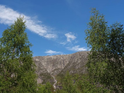 Mountain peaks under a blue sky, flanked by lush forests and fresh greenery, Eidfjörd, Norway,