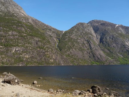 A lake surrounded by high mountains with a waterfall, blue sky and green vegetation, Eidfjörd,