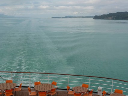 Tranquil view of the sea from the back of a ship with empty table groups and orange-coloured chairs