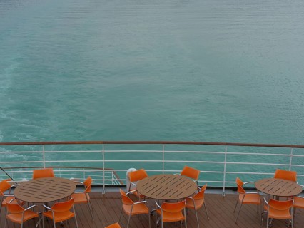 Deck of a ship with tables and chairs in orange, calm water in the background, Eidfjord, Norway,