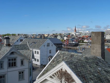 Urban scene with traditional houses, a church and water in the background under a clear blue sky,