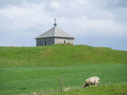 Stone church on a green hill with a grazing sheep in front of it, Haugesund, norway