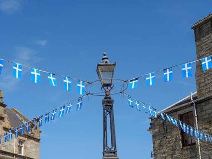 Lamp with hanging Scottish flags in front of a historic building and blue sky, Lerwick, Shetlands,