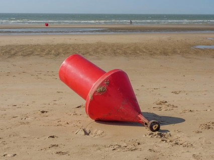 A large red buoy lies on the sand on the beach with the sea in the background, de haan, belgium