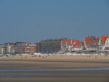 Row of buildings along a busy sandy beach with holidaymakers and calm sea in the background under a