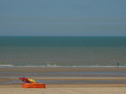 Beach with a colourful parasol and an orange and yellow striped deckchair in front of calm sea and
