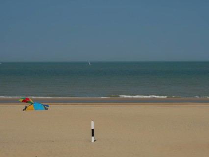 A quiet beach with a small tent in the sand, the sea in the background and a blue sky above, de