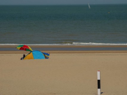 Colourful tent and parasol on a sandy beach, with calm sea in the background on a sunny day, de