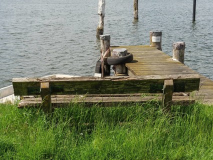 Dilapidated wooden bench at the end of a wooden footbridge leading into the water of a calm lake,