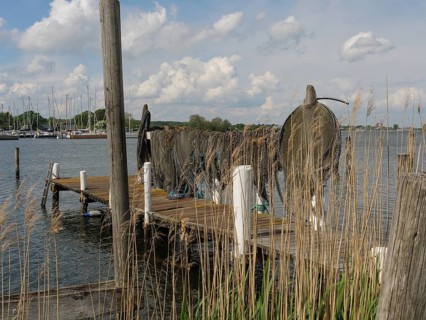 An old jetty on the lake with folded fishing nets, boats and clouds in the sky in the background,