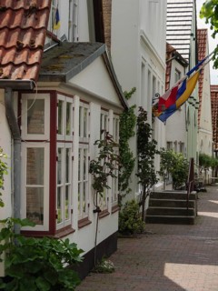 Simple residential buildings with floral decorations and a flag along a cobbled street, Kappeln,