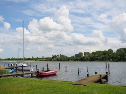 A calm harbour picture with boats at the jetty and a cloudy sky above the trees in the background,