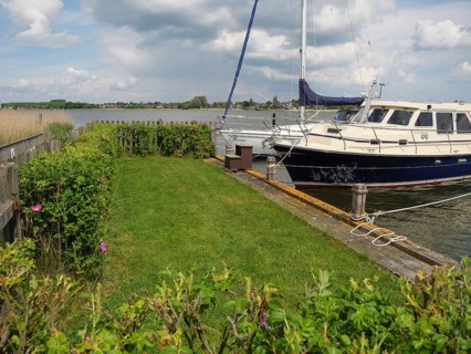 A sailing boat moored to a wooden jetty, surrounded by bushes and a cloudy sky, Arnis,