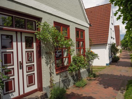 A brick-style house with red windows and a door, surrounded by plants, on a sunny day, Kappeln,