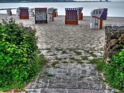 Beach chairs on a sandy beach with moss-covered cobblestones, against the backdrop of a calm sea