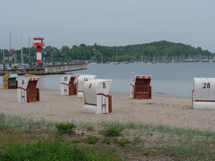 Lonely beach with numbered beach chairs and view of a lighthouse and boats in the background,