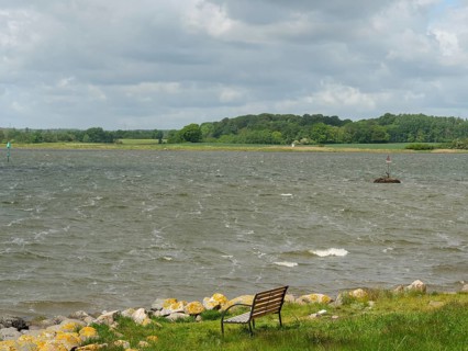 A river landscape with a bench in the foreground and a cloudy sky, Maasholm, Schleswig-Holstein,