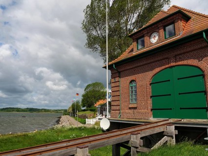 Red brick building with green Tor tor on the waterfront with railway tracks and flagpoles,