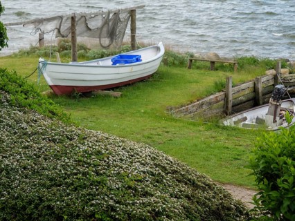 Small boat on a green bank next to the water with nets in the background, Maasholm,