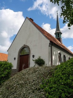 White church with high tower and red roofs, surrounded by bushes under a blue sky, Maasholm,