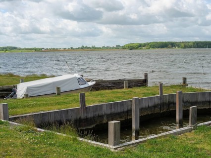 Boat in a harbour area on the water with green shore and cloudy sky, Maasholm, Schleswig-Holstein,