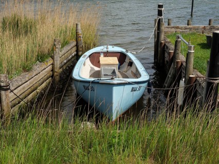 Blue boat in a narrow waterway between wooden jetties on a quiet shoreline, Maasholm,
