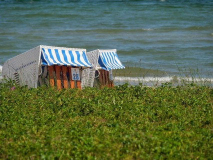 Two striped beach chairs on the beach, surrounded by grass, with the sea in the background,
