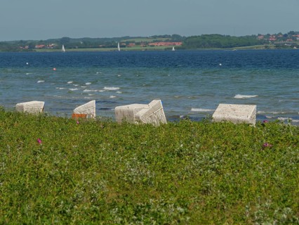 White beach chairs on the beach against the backdrop of waves and a green meadow, Flensburg,