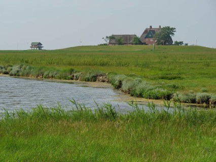 A single house stands on a small hill in the middle of a wide, green landscape near a lake, the