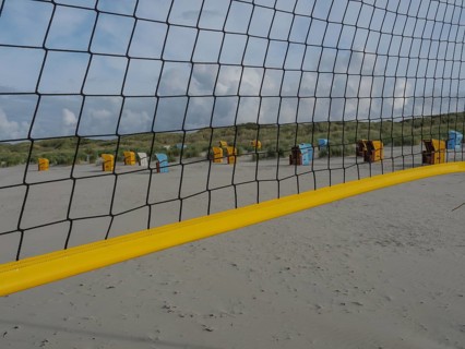 A volleyball net stretches across the beach, with dunes and beach chairs in the background, juist,