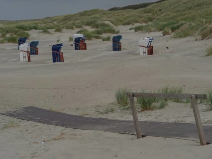 Beach with wooden path, several beach chairs and dunes, sand and cloudy sky, juist, east frisia,