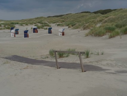 View of a beach with dunes and beach chairs in the background, wooden path embedded in the sand,