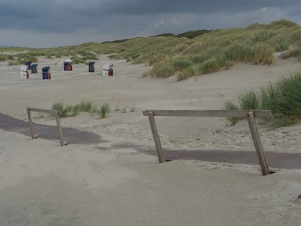 Deserted beach with a wooden path and scattered beach chairs under a cloudy sky, juist, east