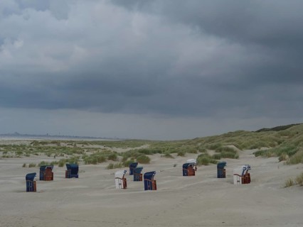 Several beach chairs scattered on the beach with dunes in the background under a grey sky, juist,