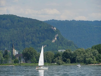 A sailing boat on a calm lake, surrounded by green hills and a church, Lindau, Lake Constance,