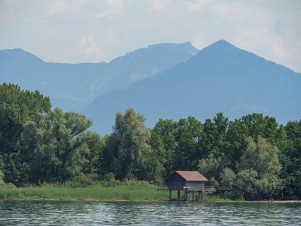 Small wooden hut on the shore of a lake, surrounded by trees with a mountain backdrop, Lindau, Lake