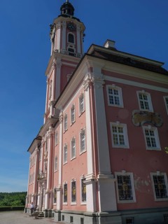 Large pink church façade with high windows under a blue sky in sunny weather, Meersburg, Germany,