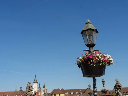 Flower hanging basket on a lantern in front of a historic backdrop and blue sky, Würzburg, Bavaria,