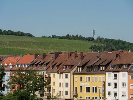 Row of colourful houses in front of green vineyards and a television tower on the horizon,