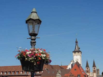 Hanging lamp with blossoming flowers in the foreground, church tower and historic buildings in the