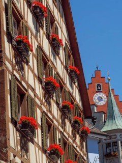 Half-timbered house with flower boxes full of red flowers and shutters, in the background a church